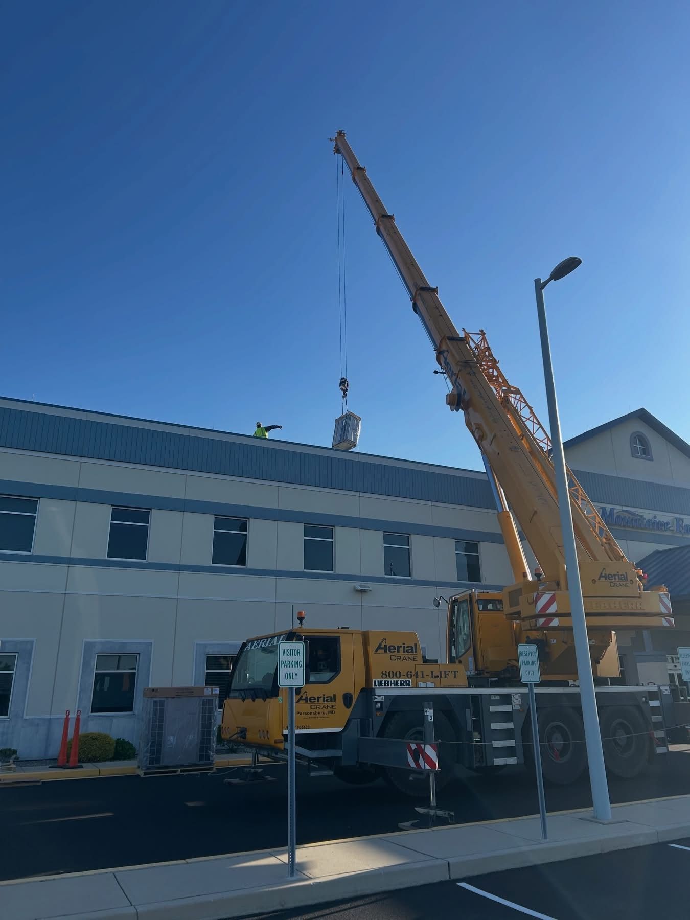 Yellow crane lifting a load beside a building under a clear blue sky