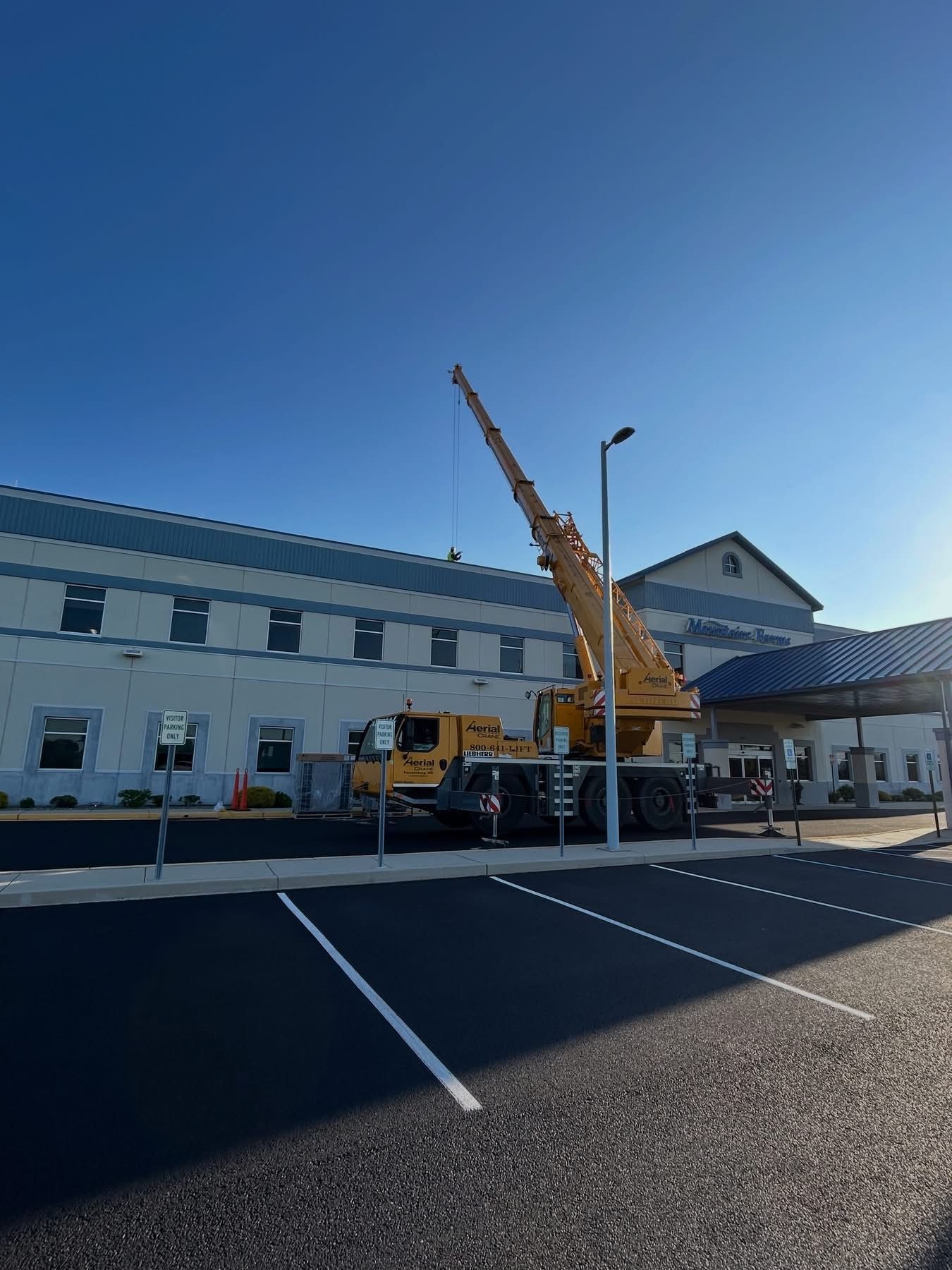 Yellow crane truck beside a white building in a parking lot under a clear blue sky