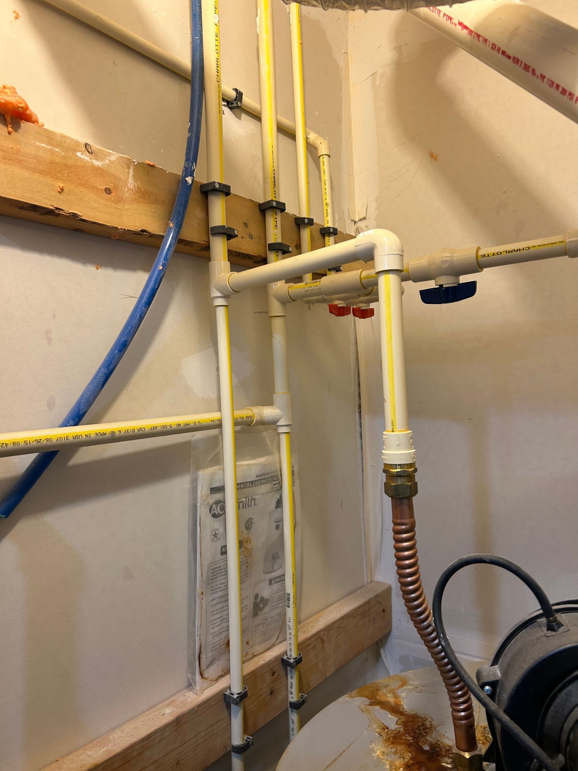 Utility pipes and valves in a basement, with white and yellow plumbing and a blue hose