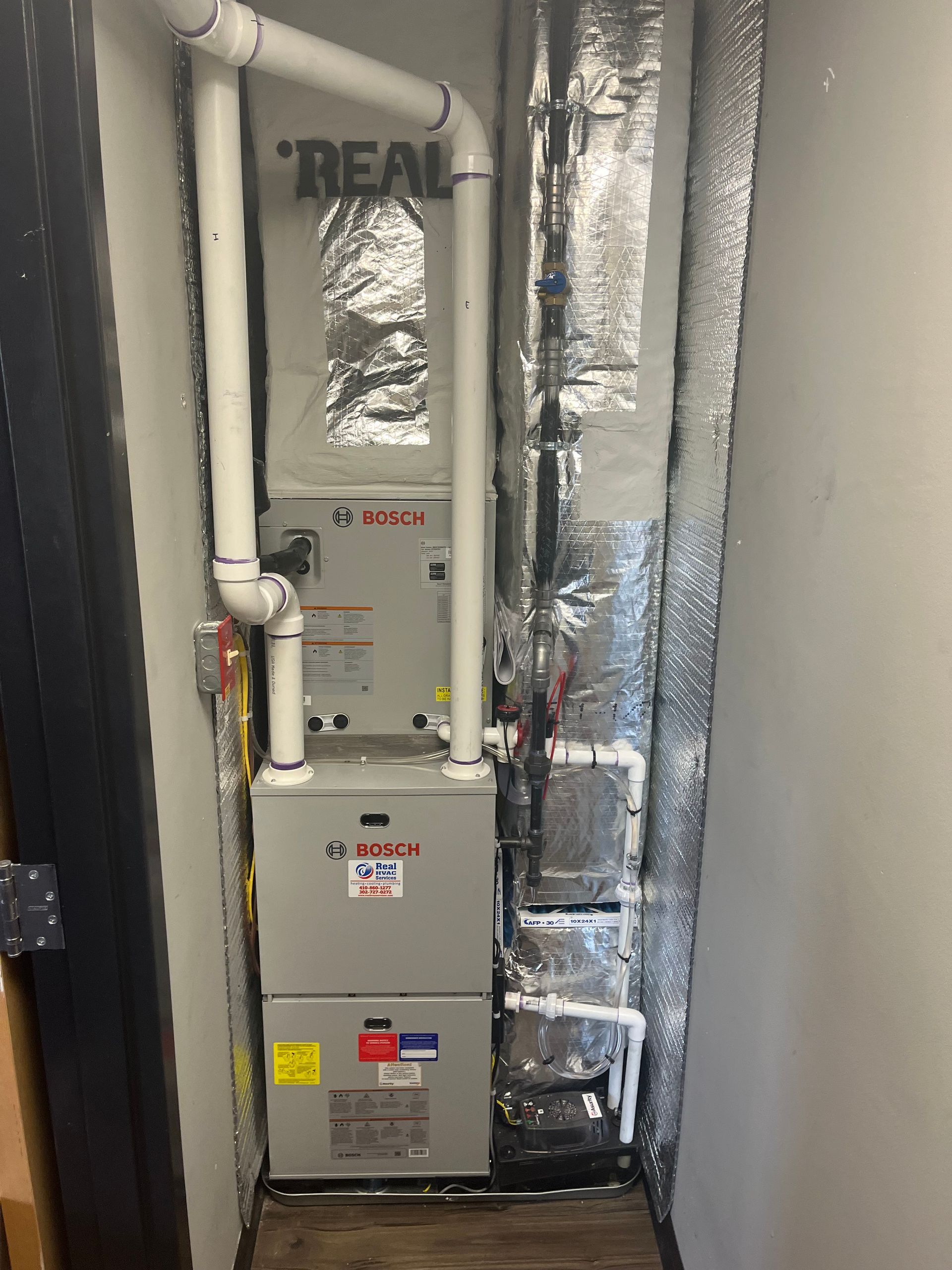 Two stacked HVAC units in a utility closet with insulated ducts and exposed piping