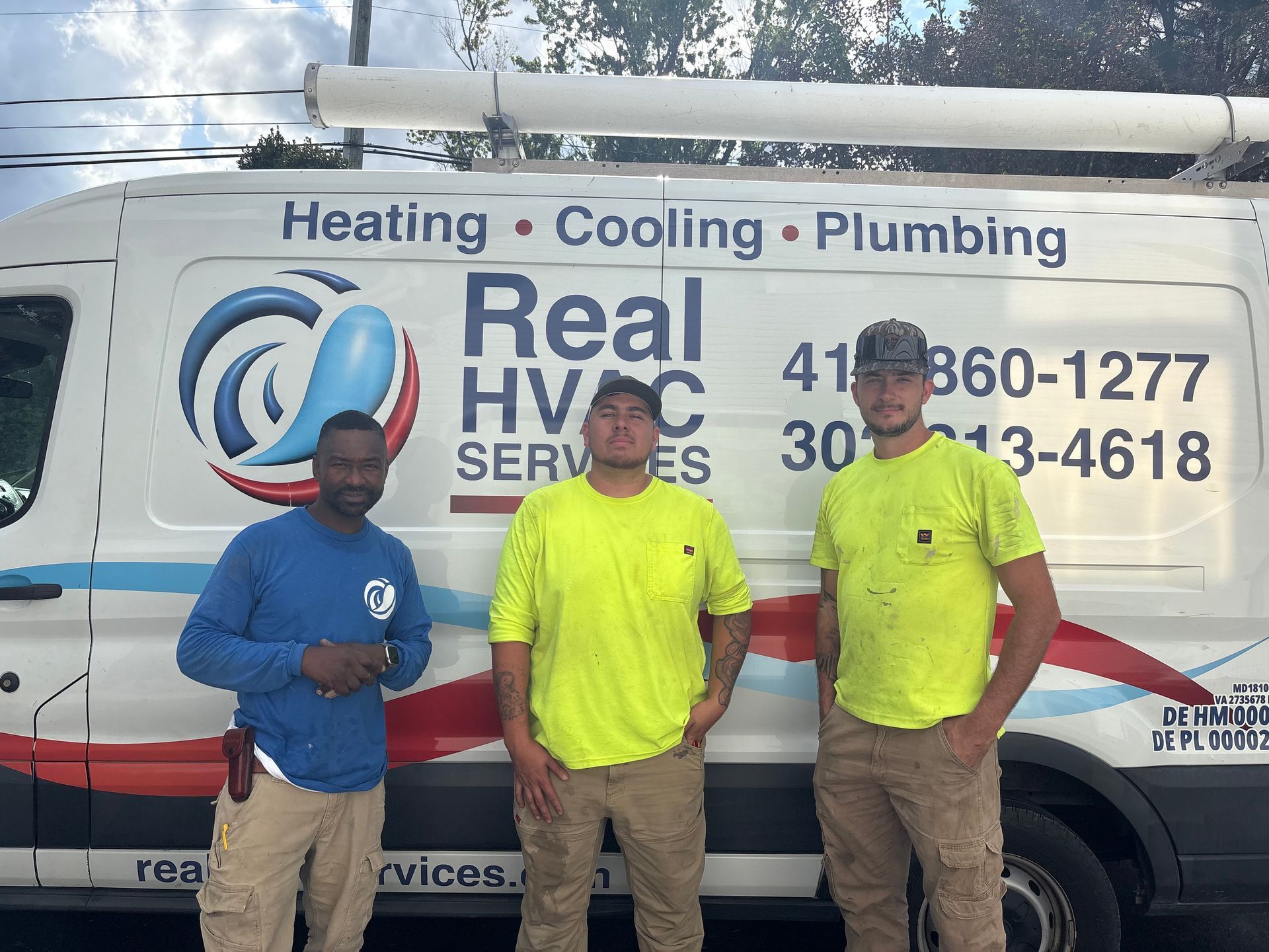Three HVAC workers stand in front of a Real HVAC Services van with company logo and phone numbers