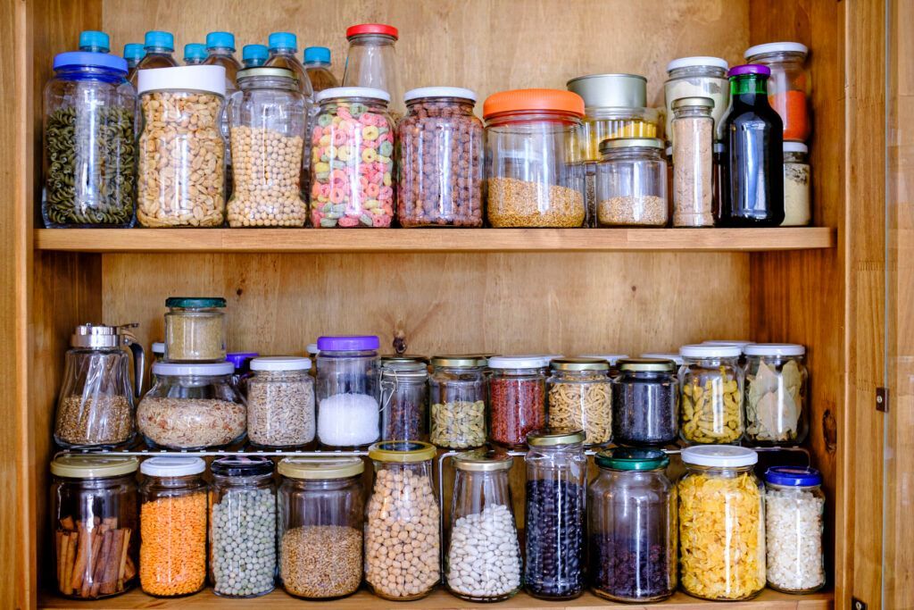 A lit up pantry with two shelves holding jars containing various food items