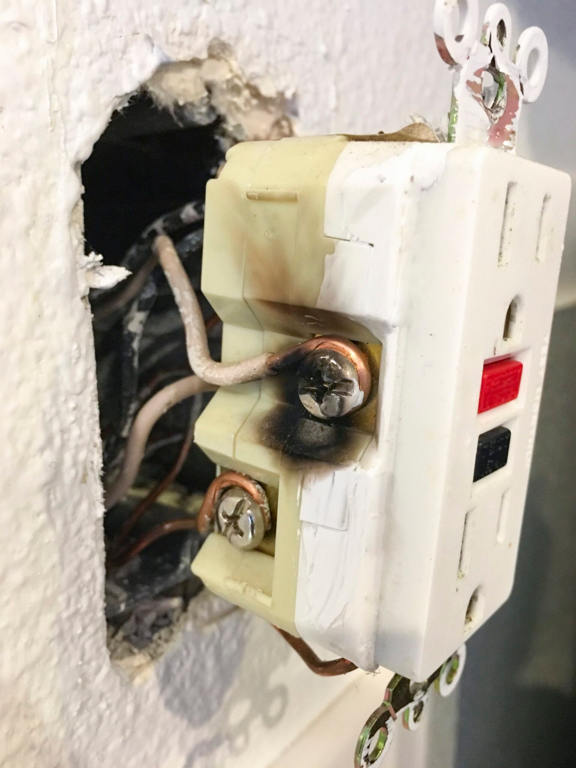 A GFCI outlet with black area from overheating. Receptacle shows the white neutral wire side.