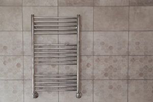 A chrome towel warmer on a tiled wall in a bathroom.
