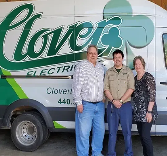 Three people standing in front of a Clover Electric service van