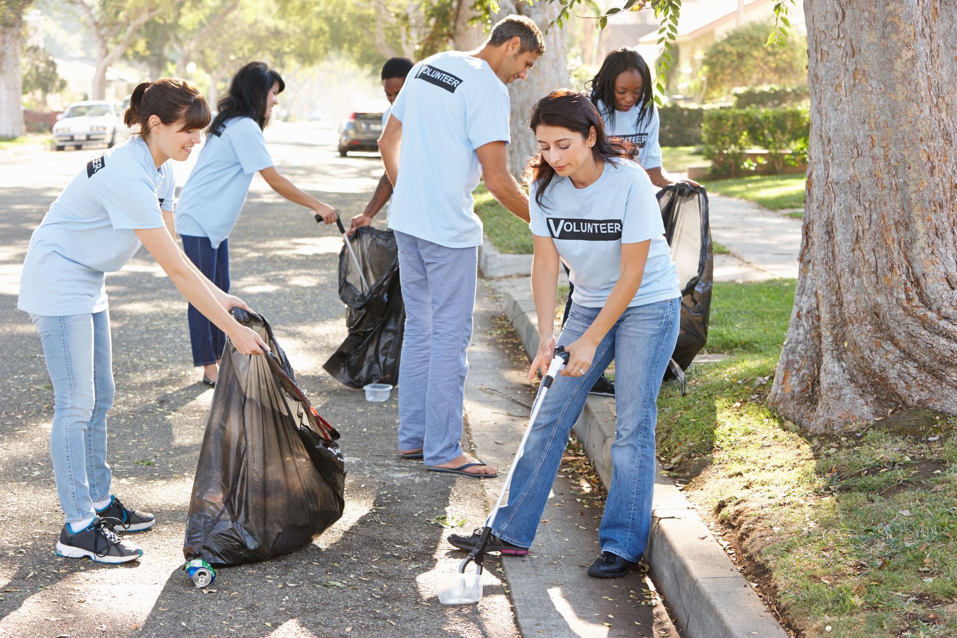 People cleaning up litter outdoors, carrying trash bags along a sidewalk near trees.