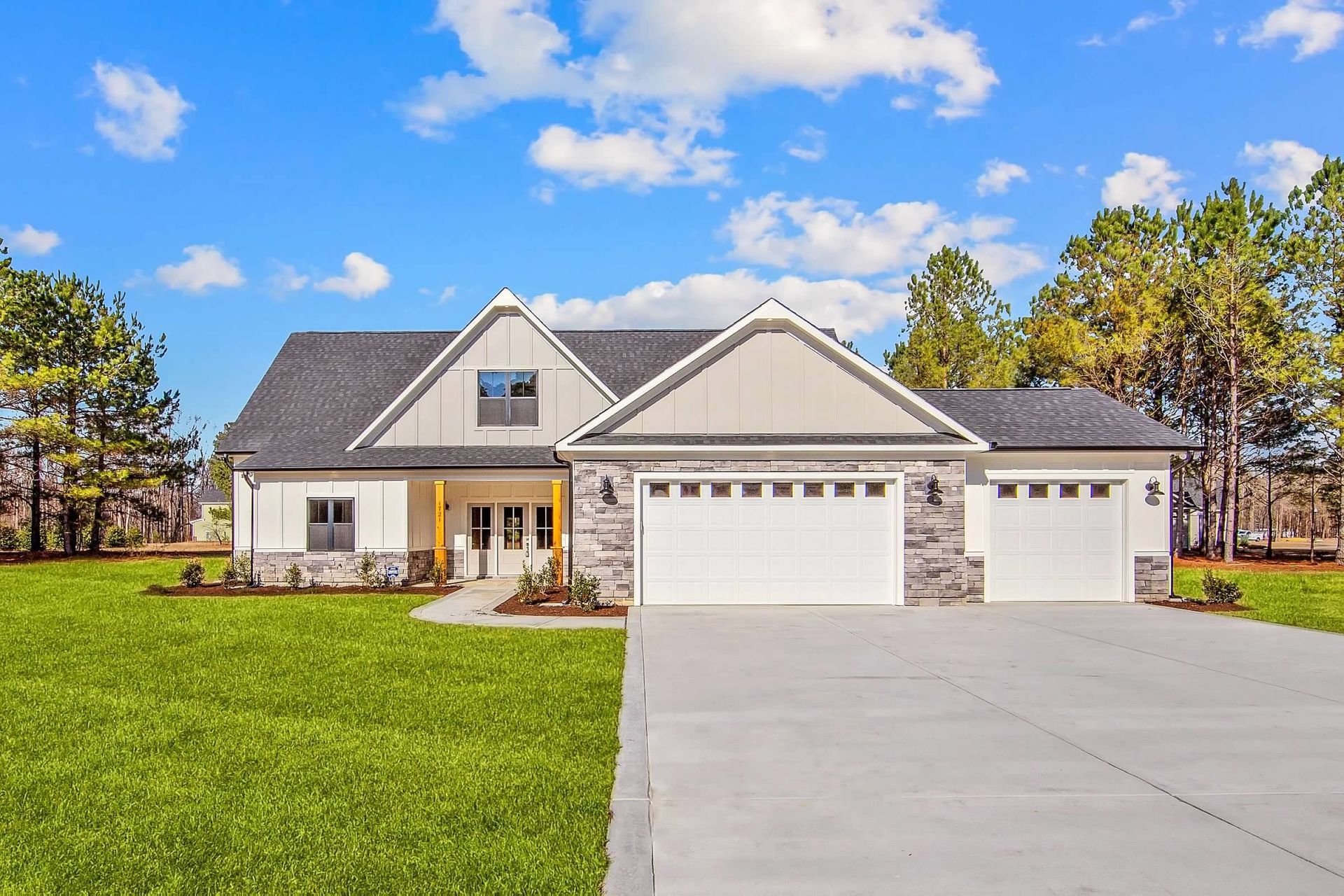 A large white house with two garage doors is sitting on top of a lush green field