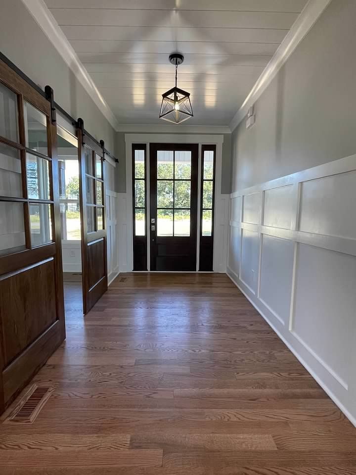 A long hallway with wooden floors and sliding barn doors leading to a door