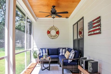 A screened in porch with a blue sectional couch and a ceiling fan.