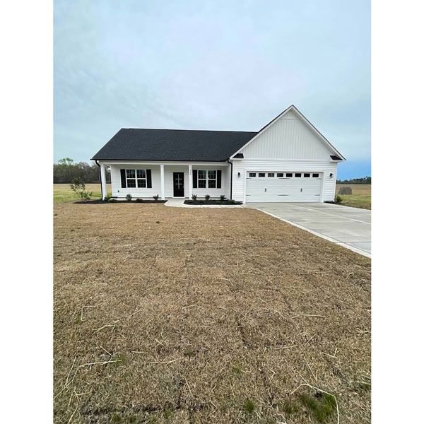 A white house with a black roof is sitting on top of a dry grass field.