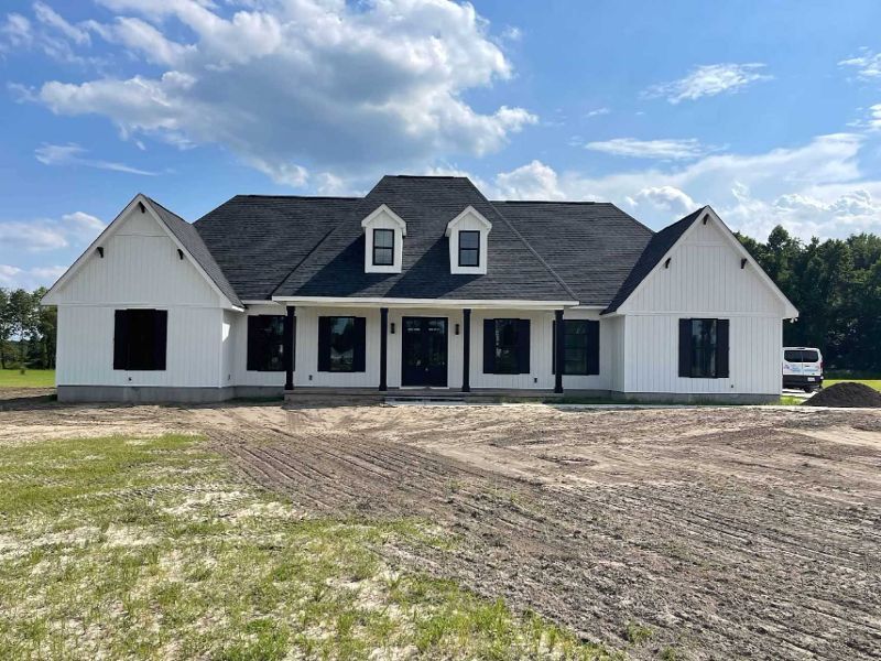 A white house with a black roof is sitting on top of a dirt field.
