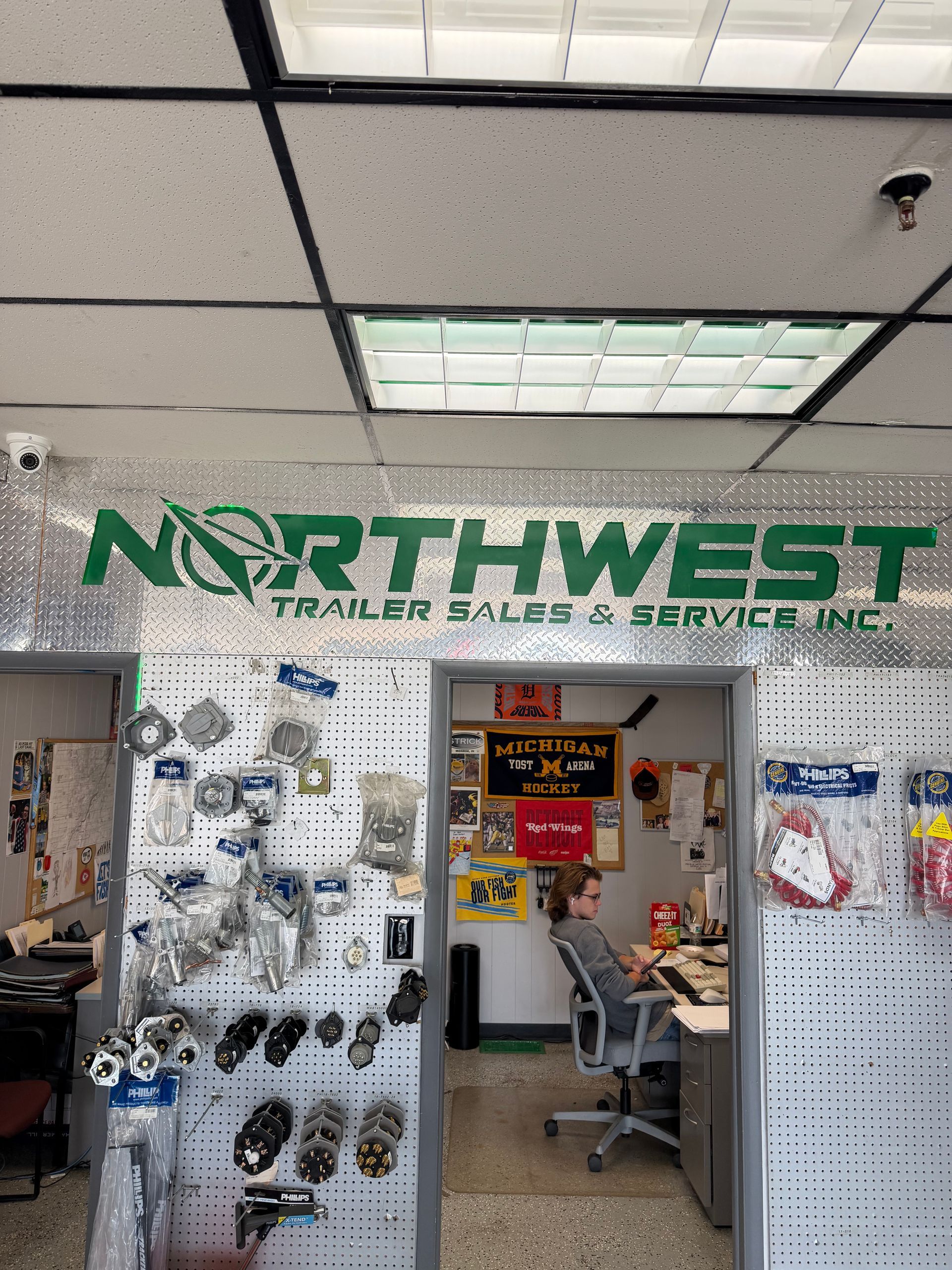Northwest Trailer Sales Service Inc. storefront with displays of trailer parts and a seated person inside
