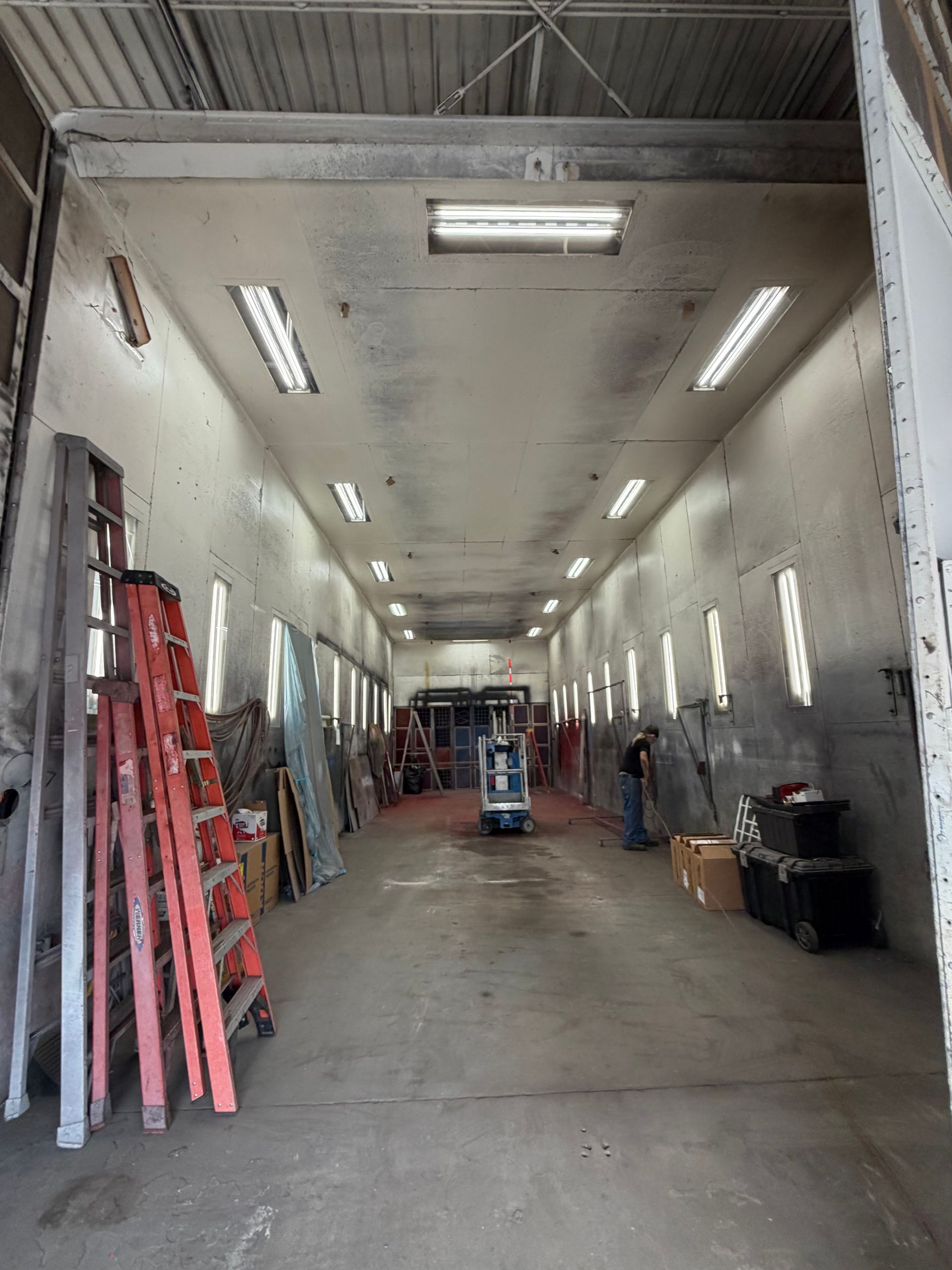 Long industrial workshop with ladders, tools, and supplies along the walls