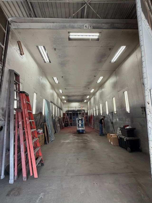 Long narrow workshop with white walls, fluorescent lights, ladders, and equipment along the sides