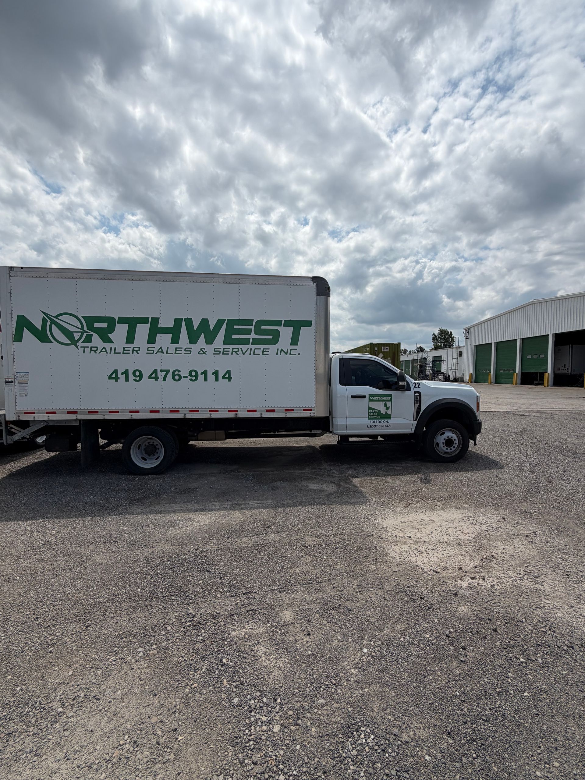 White Northwest moving truck parked on gravel under a cloudy sky, with green buildings in the background