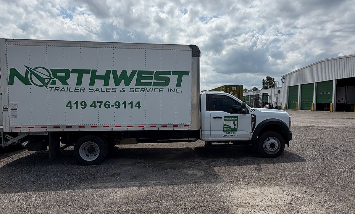 Northwest moving truck parked on gravel beside a warehouse under cloudy skies