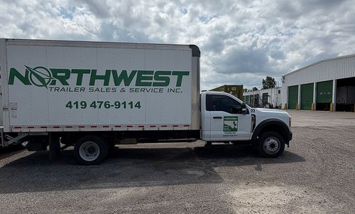 Northwest moving truck parked on gravel beside a warehouse under cloudy skies