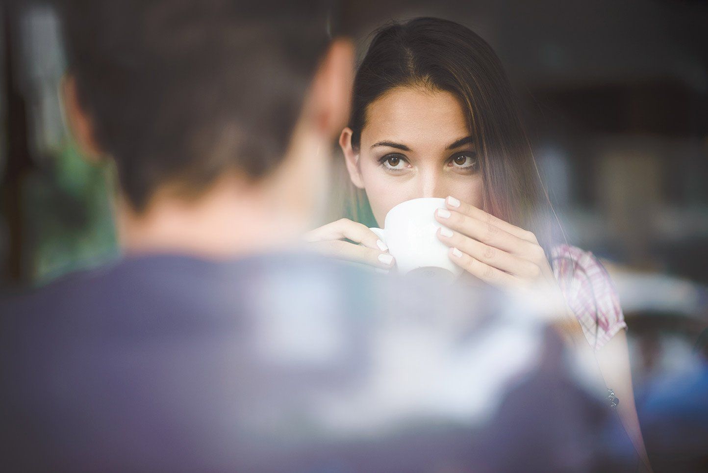 A woman gazes at a male companion over her coffee cup.