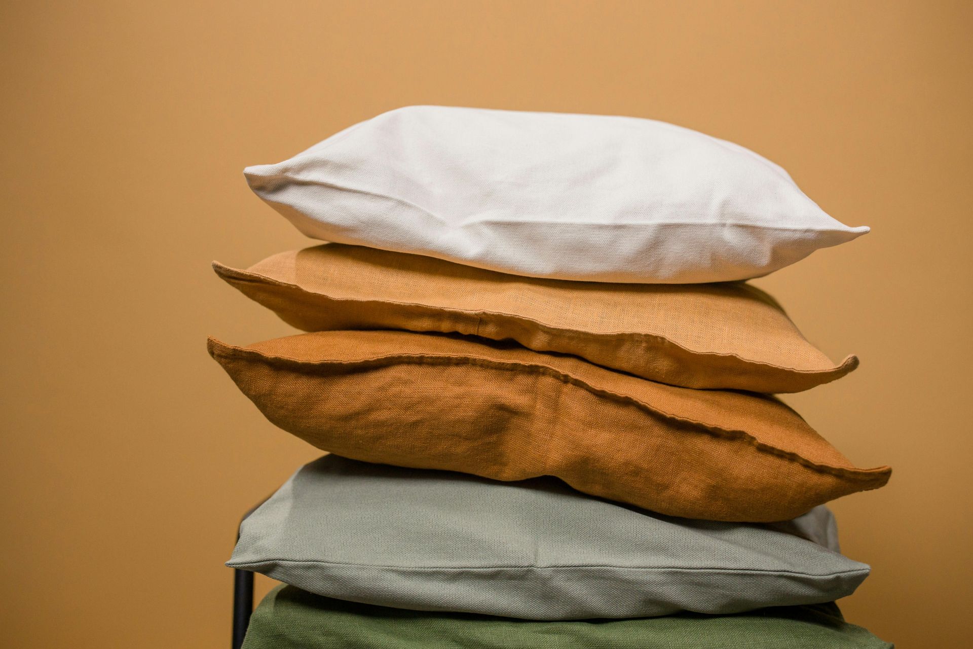 Four pillows in various earth tones stacked on each other against a neutral backdrop.
