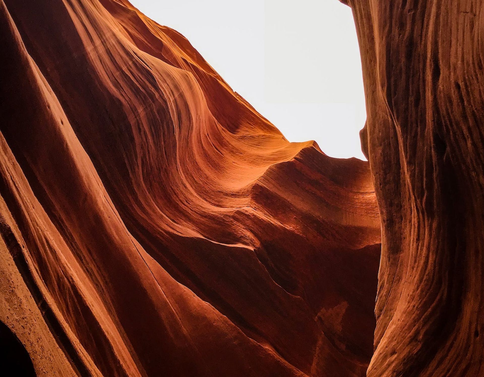 Red sandstone canyon walls with sunlight creating flowing patterns and a bright sky opening above