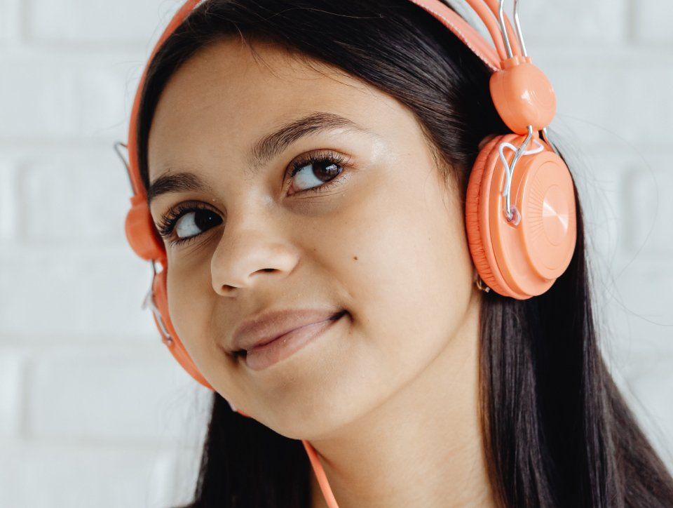 Person with dark hair wearing orange headphones, looking up and smiling slightly.