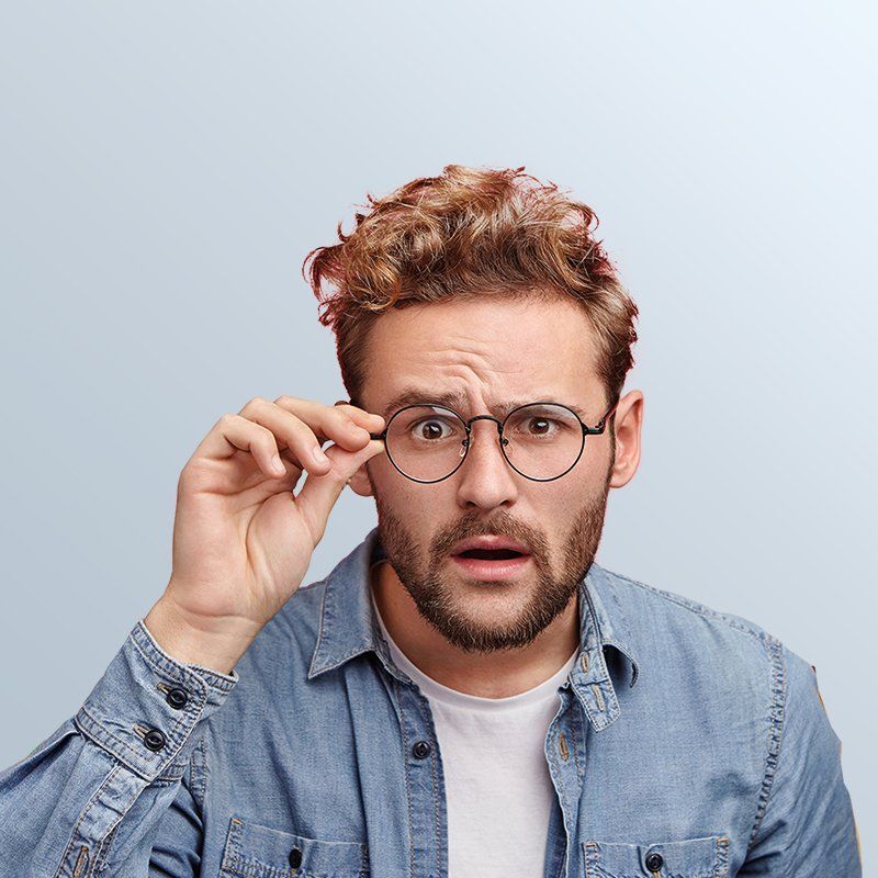 Man with curly brown hair and glasses, surprised expression, adjusts his glasses.