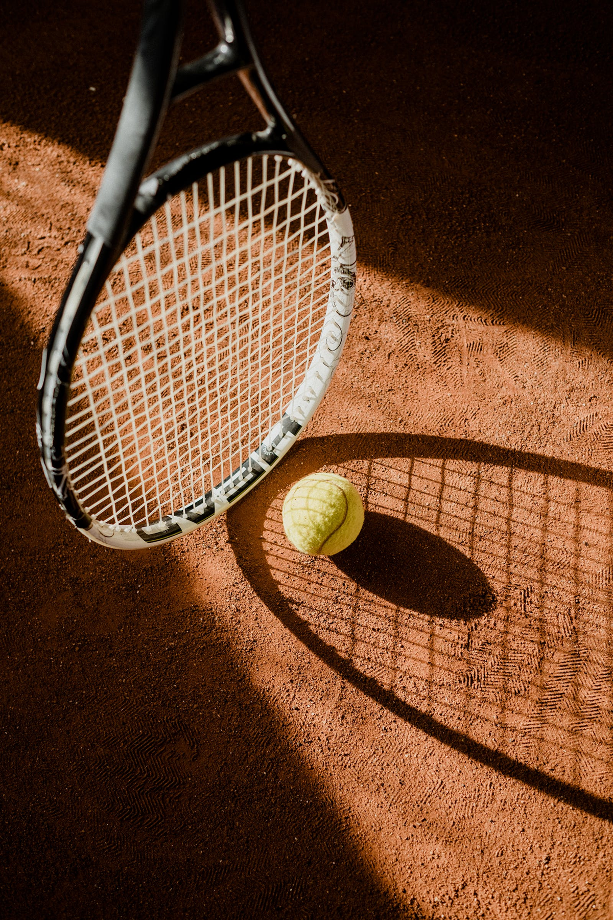 Tennis racket and ball on a clay court in warm sunlight