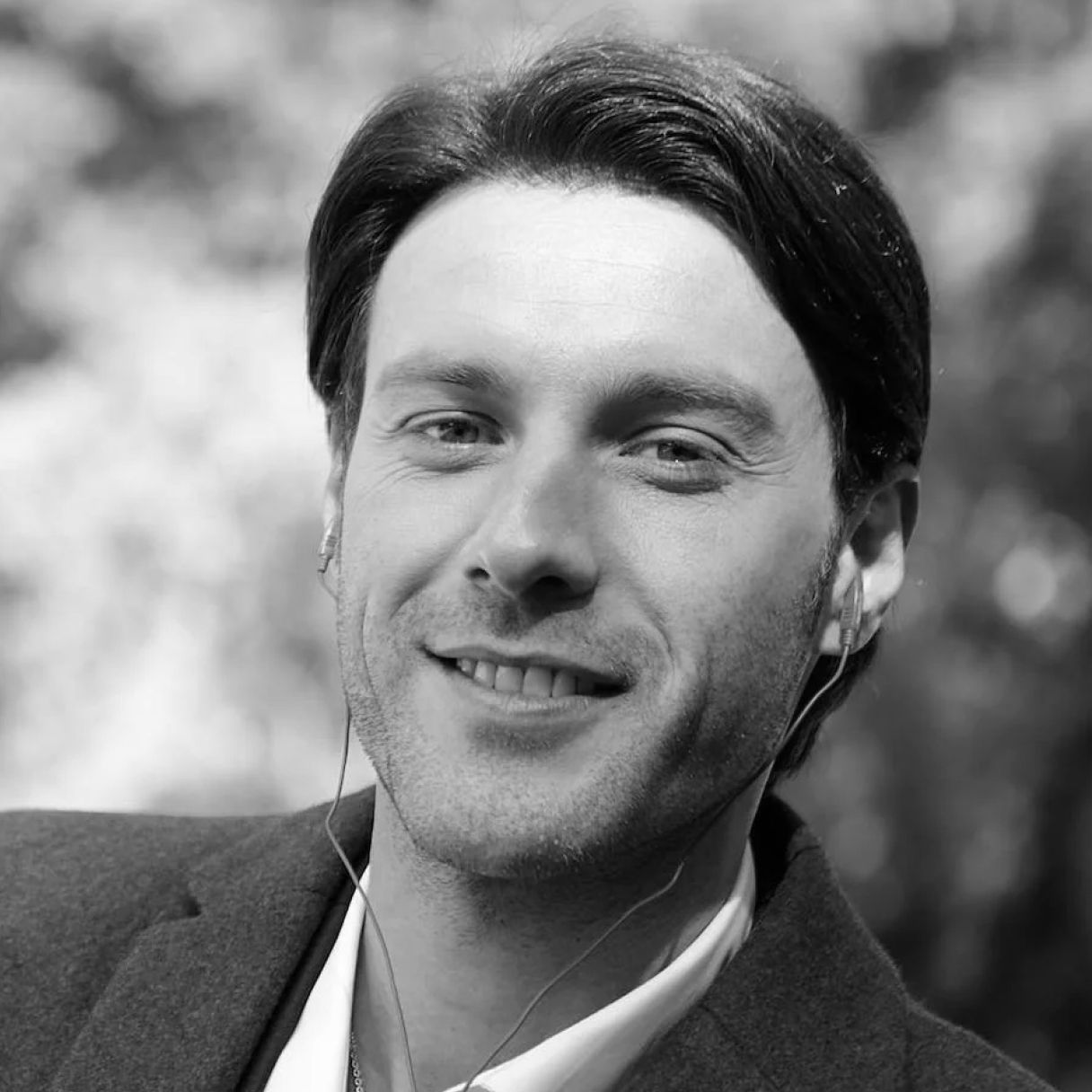 A man wearing headphones and a suit is smiling in a black and white photo.