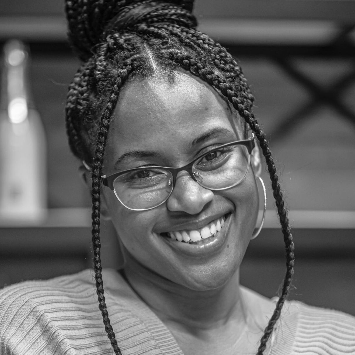 A woman with braids and glasses is smiling in a black and white photo.